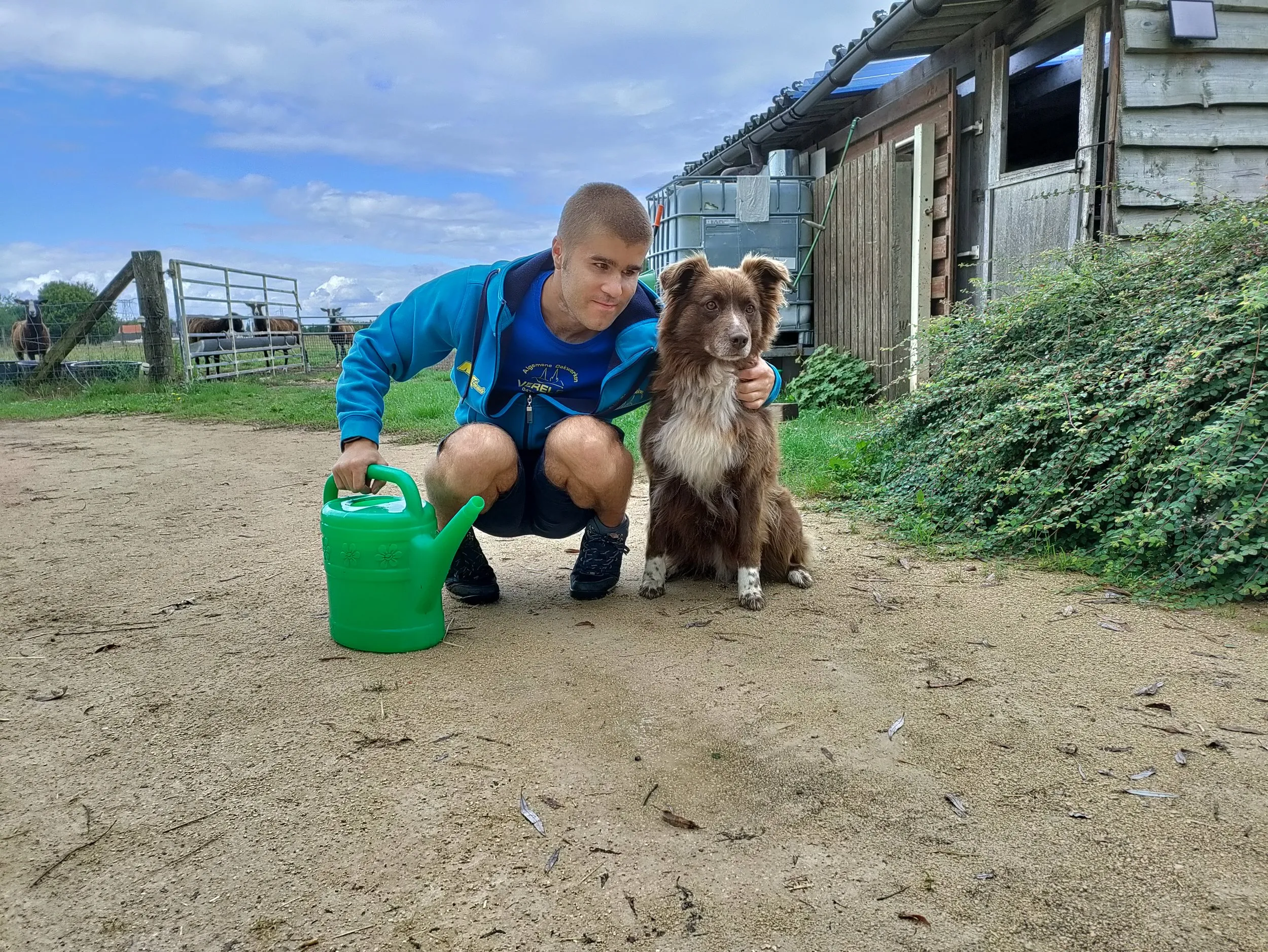 Een jongeman met gieter en hond op het erf
